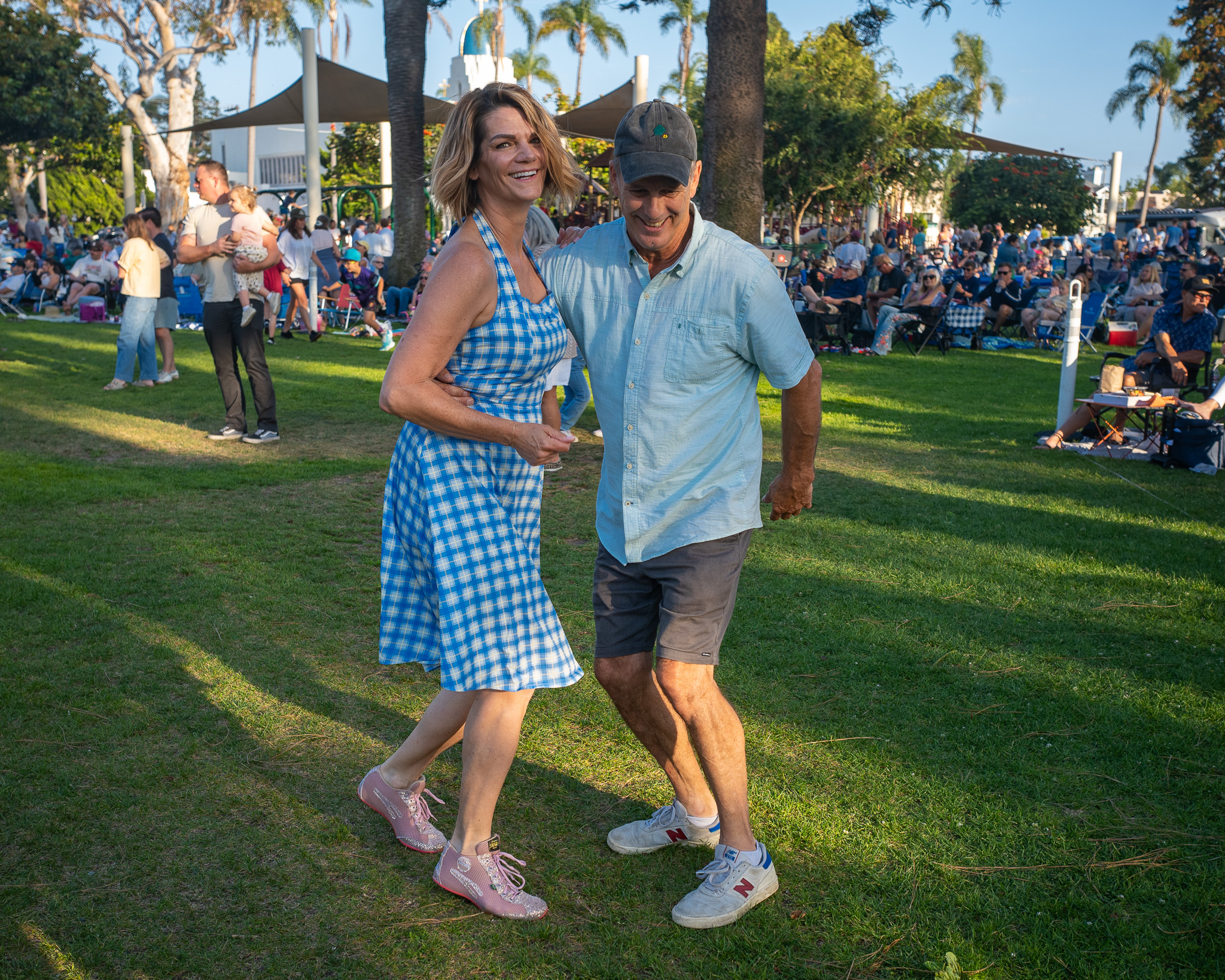 A smiling couple dance arm-in-arm on the grass at an outdoor concert.